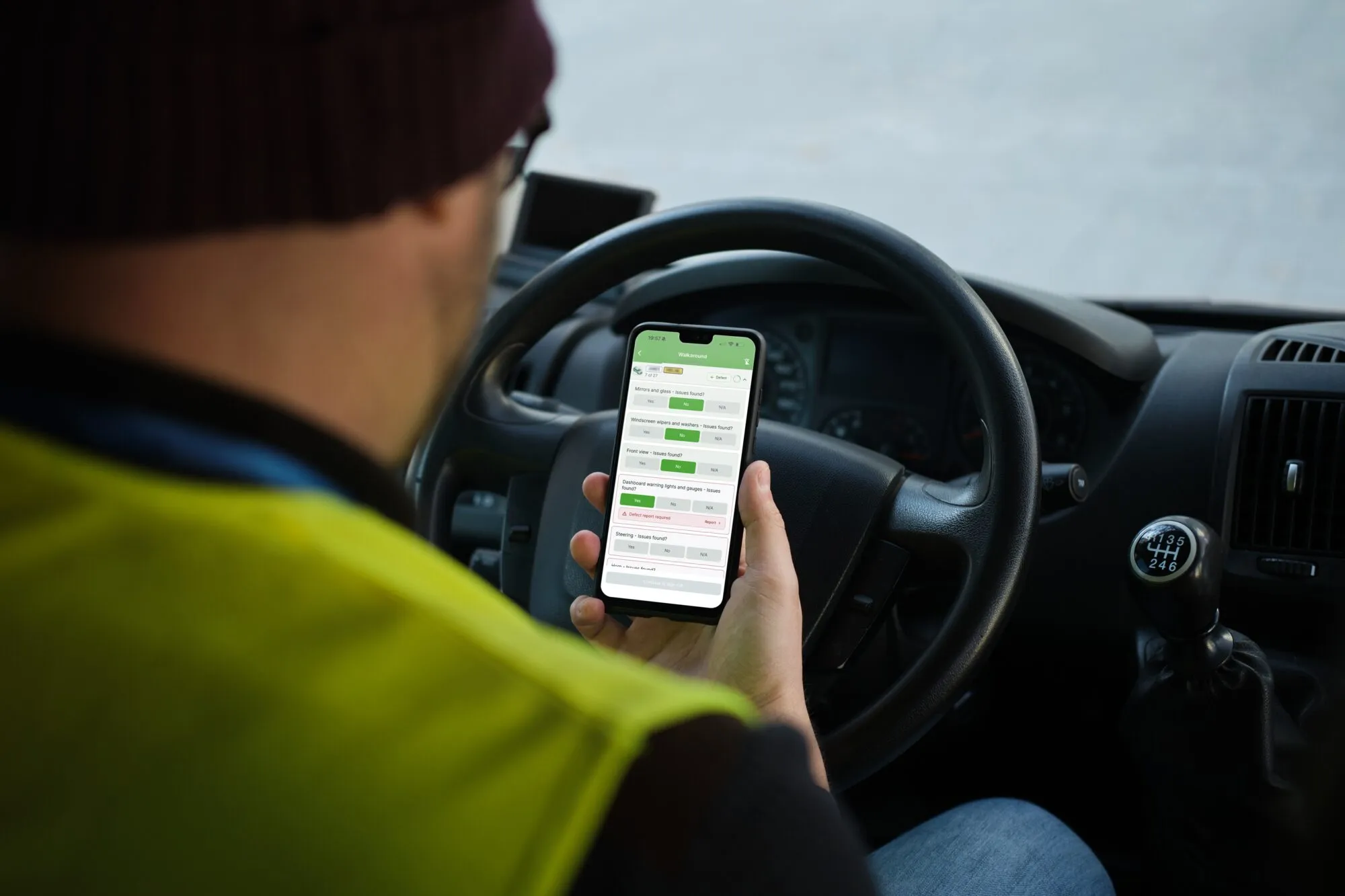A driver in a hi-vis vest completing a DVSA walkaround inspection on the OnPoint app in the cab