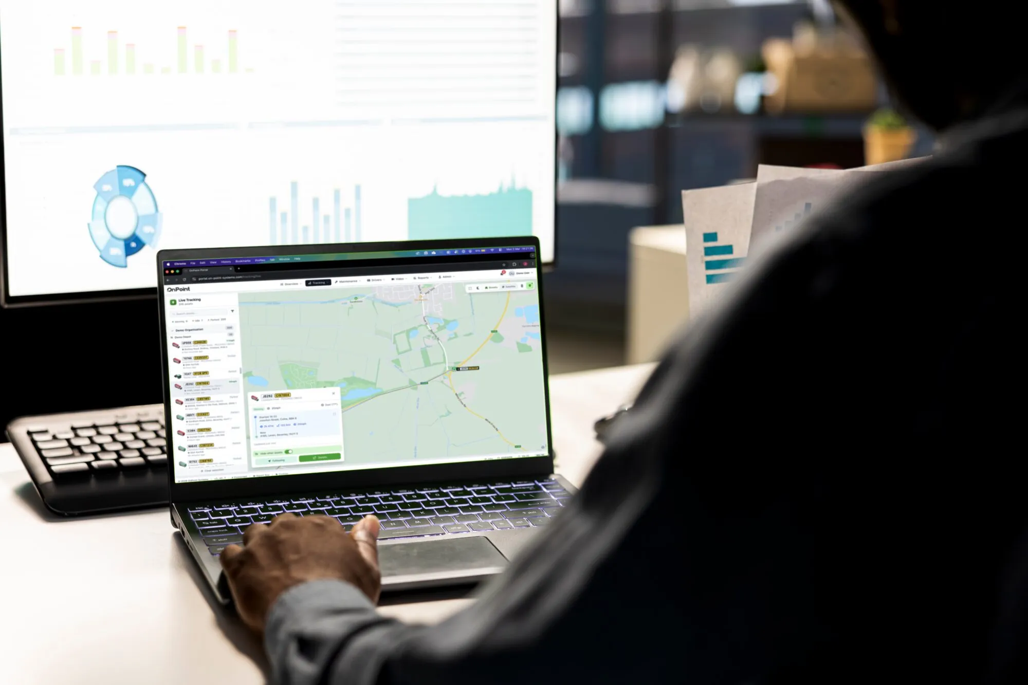 A fleet manager monitoring the OnPoint live-tracking portal on a laptop and desktop in the office